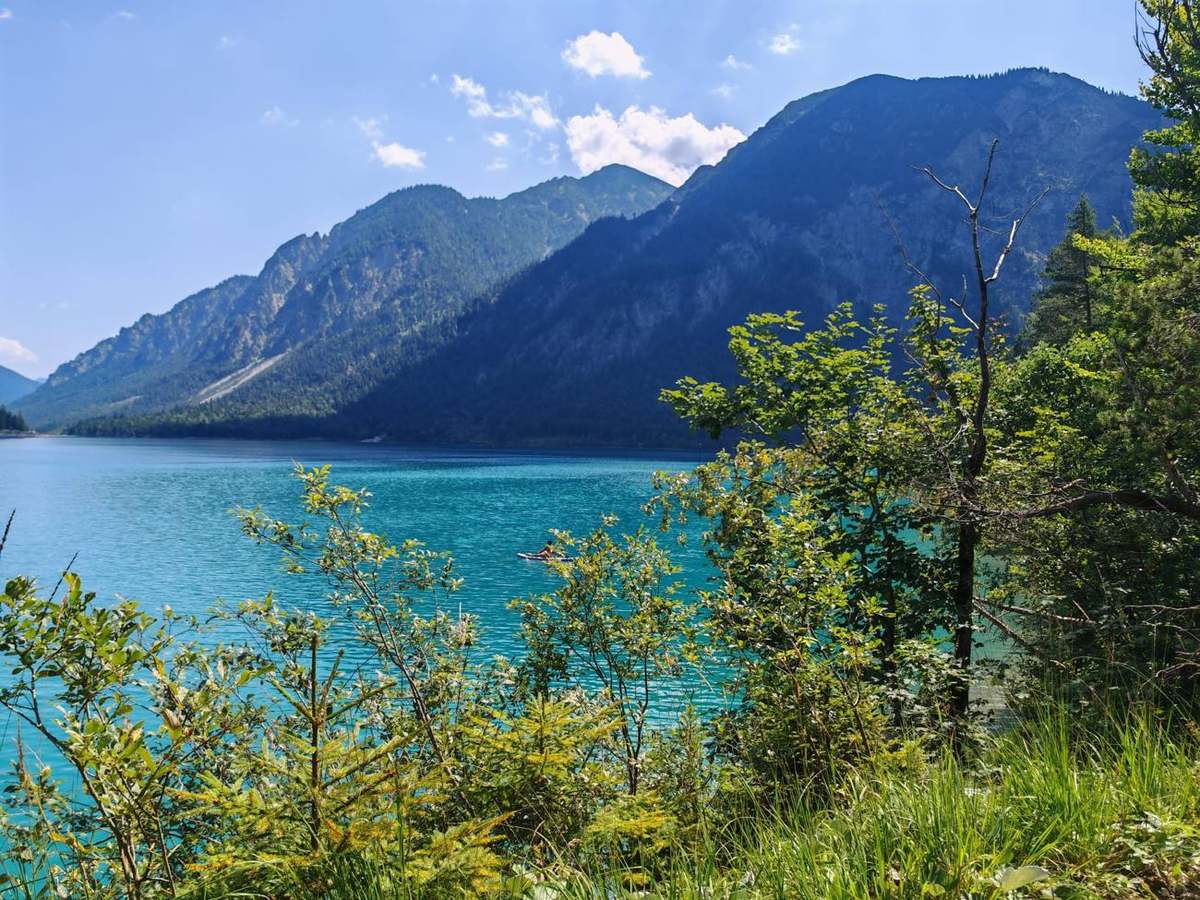 Türkisblauer See mit Bergen und einer Person auf dem Stand-up-Paddle-Board
