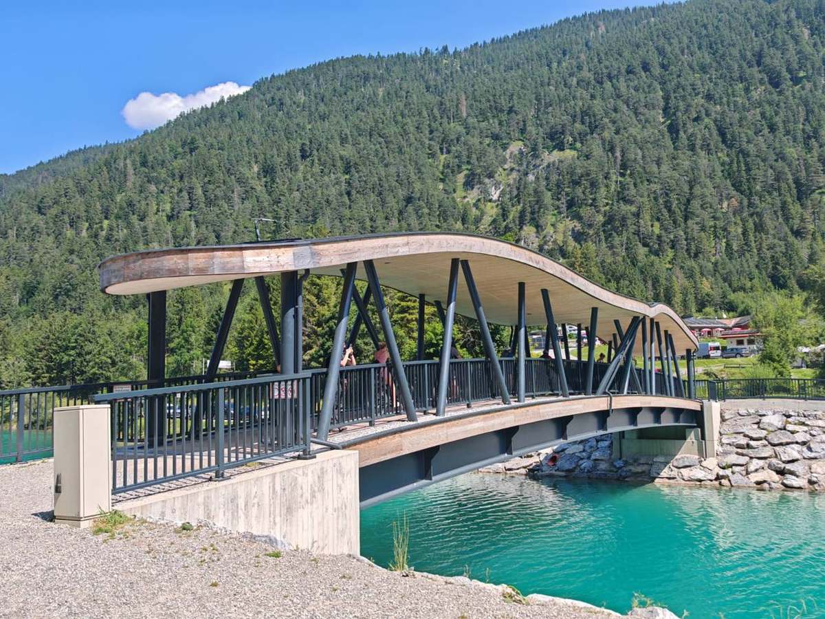 Geschwungene Holzbrücke am türkisblauen See
